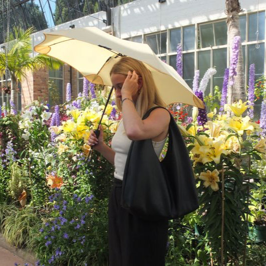 Woman holding a large yellow umbrella in a garden with colourful flowers and plants.