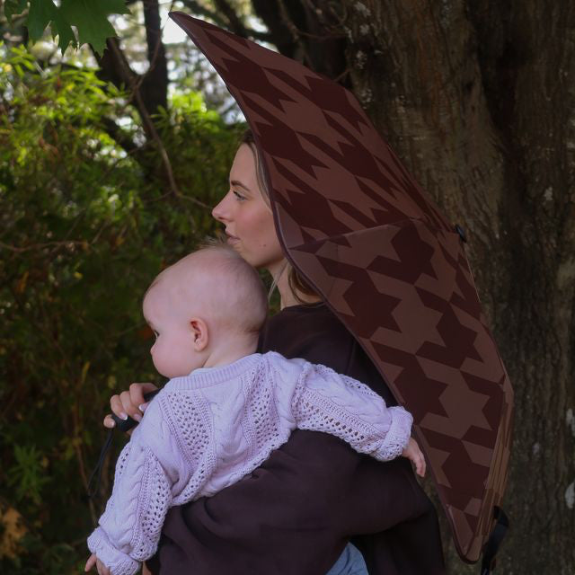 Woman holding a baby and a patterned umbrella in a forest setting